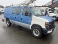 A 2009 Ford Econoline van with a blue and white exterior featuring a ladder rack on top and large tires