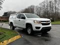 A white 2018 Chevrolet Colorado pickup truck with a cap on the bed parked at an angle on a wet surface