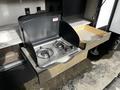 A slide-out outdoor kitchen featuring a two-burner gas stove and a wooden storage drawer next to it