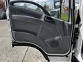The image shows the open driver's door of a 2016 Isuzu NQR featuring a gray interior with controls and a speaker grille