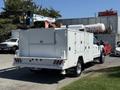 A 2024 Ford F-550 Super Duty with a white service body and a hydraulic lift mounted on top for maintenance and utility work