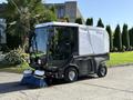A 2017 Madvac LS100 street sweeper with a compact design featuring a clear cab a white body and blue brushes on the front