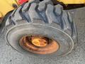 A large, worn black tire of a 2007 Komatsu WB156PS-5 featuring deep treads and rusted wheel rim