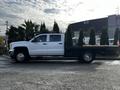 A white 2017 GMC Sierra 3500HD with a flatbed design parked on a surface surrounded by greenery