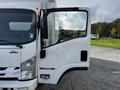 A 2016 Isuzu NPR with an open driver's side door showcasing the vehicle's white exterior and sleek design