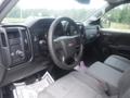 The interior of a 2015 Chevrolet Silverado 1500 featuring a black dashboard with gauges a steering wheel with the Chevrolet logo and gray fabric seats