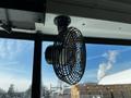 A metal circular fan mounted to the ceiling of a vehicle with black wire mesh surrounding the blades
