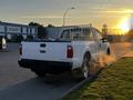 A white 2012 Ford F-250 pickup truck with a bed rack visible from the rear parked on a street with steam rising from the exhaust