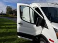 A 2020 Ford Transit with an open front driver's door showcasing its white exterior and side mirror setup