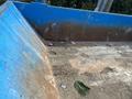 A 2002 Ford F-550 pickup truck parked near a large blue dumpster filled with dirt and debris