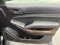 Interior door panel of a 2016 Chevrolet Tahoe featuring a black leather finish with wood accents and a control panel for windows and locks