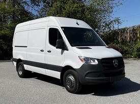 A 2022 Mercedes-Benz Sprinter van in white with a black front bumper and steel wheels parked with its side facing the viewer