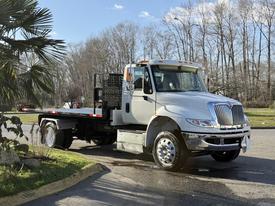 A 2017 International 4300 truck with a flatbed and silver body is parked at an angle showcasing its front and side view