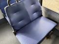 A blue padded seat with textured upholstery and metal armrests inside a vehicle