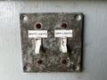 A weathered electrical switch plate with two labeled switches for white lights and safe lights