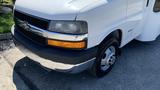 A 2011 Chevrolet Express with a white exterior a chrome grille and headlights visible along with a front tire on a clean surface