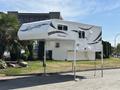 A 2018 Westland Travelaire truck camper with a sleek white exterior and decorative graphics is mounted on retractable legs