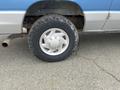 A close-up of a silver wheel with a rugged tire on a blue Ford Econoline van