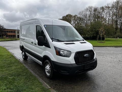 2021 Ford Transit van in white with black accents parked on a wet surface showcasing its front and side features