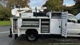 A side view of a white 2007 Ford F-550 with an attached aerial lift and open storage compartments on the side