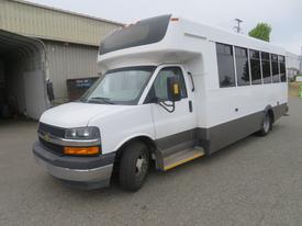 A 2020 Chevrolet Express shuttle bus with a white body and gray lower panel featuring large windows and a front entry step