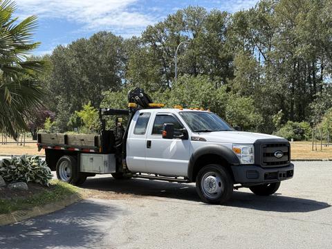 A 2012 Ford F-450 Super Duty pickup truck with a flatbed and a crane attachment parked on a street