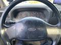 Steering wheel of a 2002 Ford F-550 with the Ford logo centered and various dashboard gauges visible in the background