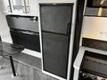 A black two-door refrigerator with a sleek design located in a kitchen space of a 2022 Heartland Torque