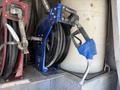 A blue fuel nozzle attached to a black hose on a reel mounted on a vehicle with a white fuel tank in the background