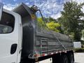 A 2010 Freightliner M2 106 dump truck with a metal bed and a raised hydraulic lift mechanism on the side