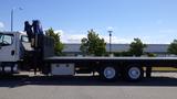 A 2017 Freightliner M2 106 flatbed truck with a black bed and extended crane on the back parked on the street