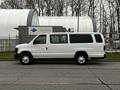 A white 2011 Ford Econoline van parked on the street with sliding side doors and large windows