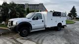 A 2007 Ford F-550 utility truck with a white body and black accents featuring storage compartments and warning lights on top