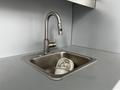 A stainless steel sink with a modern faucet containing a few discarded coffee cups inside