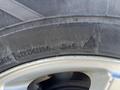 A close-up of a tire mounted on a silver alloy wheel with markings indicating tire specifications and performance ratings