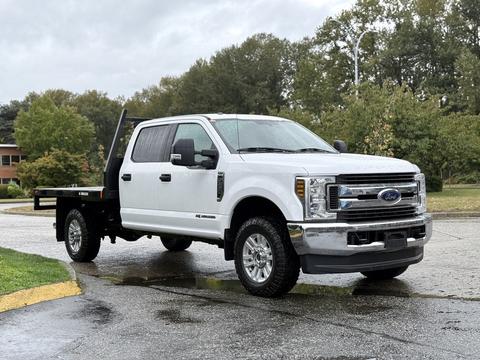 A 2019 Ford F-350 Super Duty truck with a white cab and black flatbed parked at an angle with prominent wheels and chrome grille