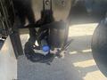 Close-up of a hydraulic component featuring a black cylindrical body with silver connections and a blue fitting mounted on a truck chassis