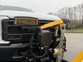 A 2023 Ford F-250 with a yellow snow plow attached to its front featuring a chain and lever mechanism