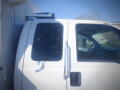 A white 2005 Ford F-750 truck's cab featuring a large window and side mirror with the driver's door partially open