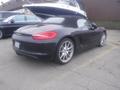 A black 2016 Porsche Boxster with a convertible top and sleek body design parked with a yacht in the background