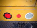 Close-up of a yellow freightliner MT45 chassis showing three distinct lights: a red circular light a circular red reflector and a circular clear lens light