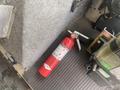 A red fire extinguisher is lying on a textured surface inside a vehicle with a silver metal panel nearby