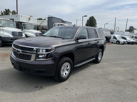 A 2016 Chevrolet Tahoe in dark gray with chrome accents and silver wheels parked on a lot