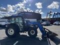 A blue 2010 New Holland T4050 tractor with a front loader attachment parked with large tires and a dual-cab structure