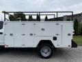 A side view of a white 2020 Ford F-550 with a utility body featuring multiple compartments and a black rack on top