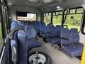 Interior of a 2020 Chevrolet Express bus featuring rows of blue upholstered seats with armrests and a spare tire on the floor