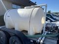 A large white tank mounted on a black trailer connected to a pump with hoses extending from the tank