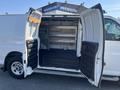 A 2016 GMC Savana van with its double rear doors open revealing a spacious interior with metal shelving and a rubber floor mat