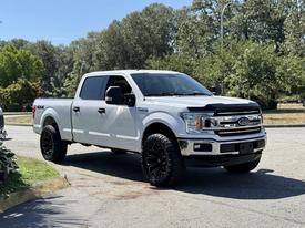A 2018 Ford F-150 in white with a black grille and large black wheels parked on a driveway
