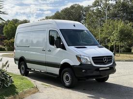 A 2017 Mercedes-Benz Sprinter van in a light color with a high roof and cargo area, featuring black trim and black wheels